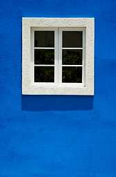 A white, divided window sits in a bright tropical blue stucco wall in Barbados.